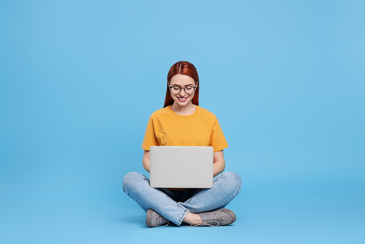 2291416847 Smiling,Young,Woman,Working,With,Laptop,On,Light,Blue,Background
